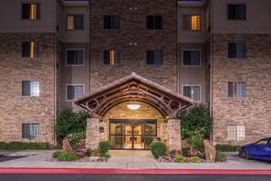 A multi-story building with a stone facade, a central entrance with a wooden archway, and a blue car parked in front. - Staybridge Suites Las Cruces by IHG (Las Cruces)