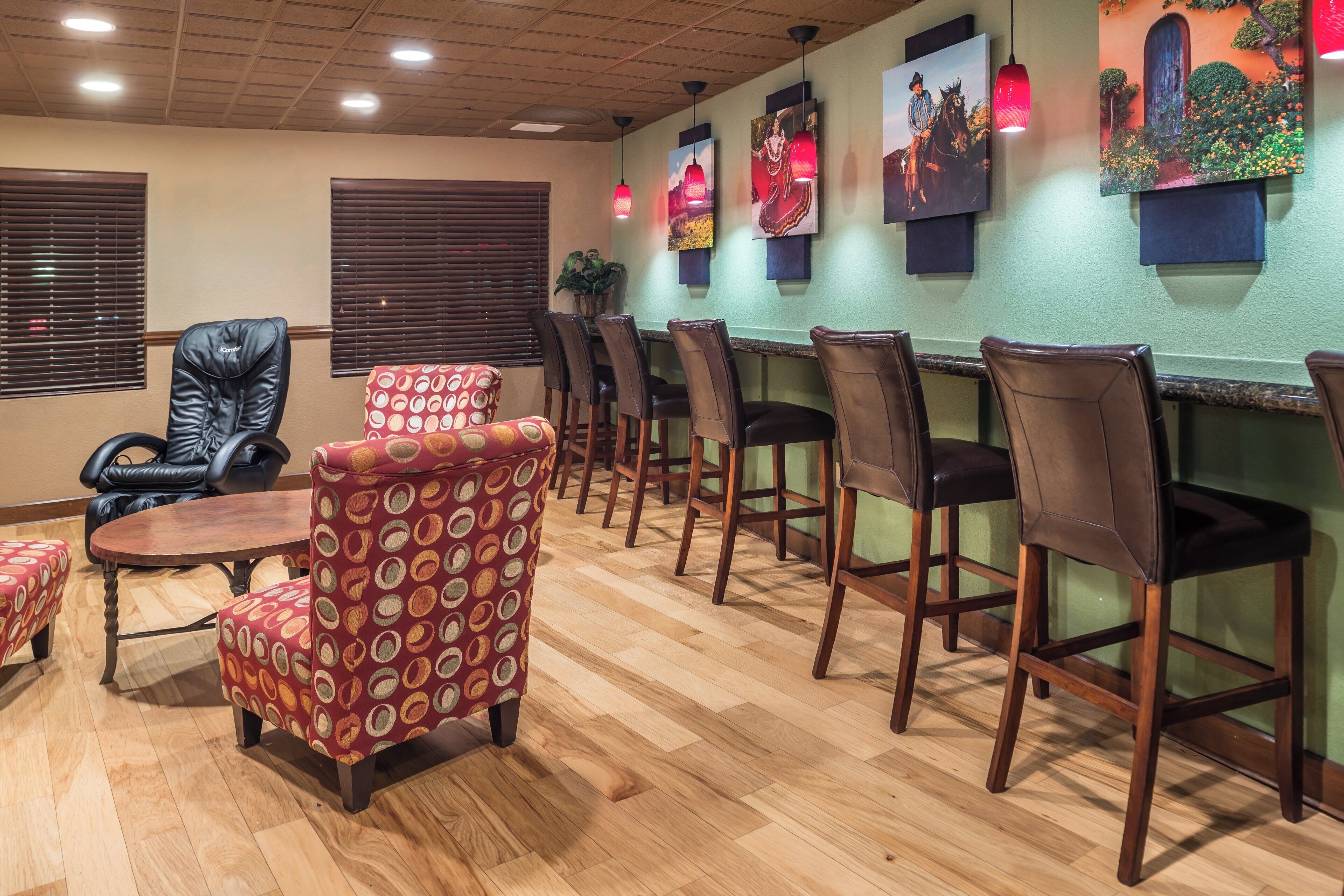 A restaurant interior with wooden flooring, leather chairs, a patterned ottoman, and wall-mounted artwork.