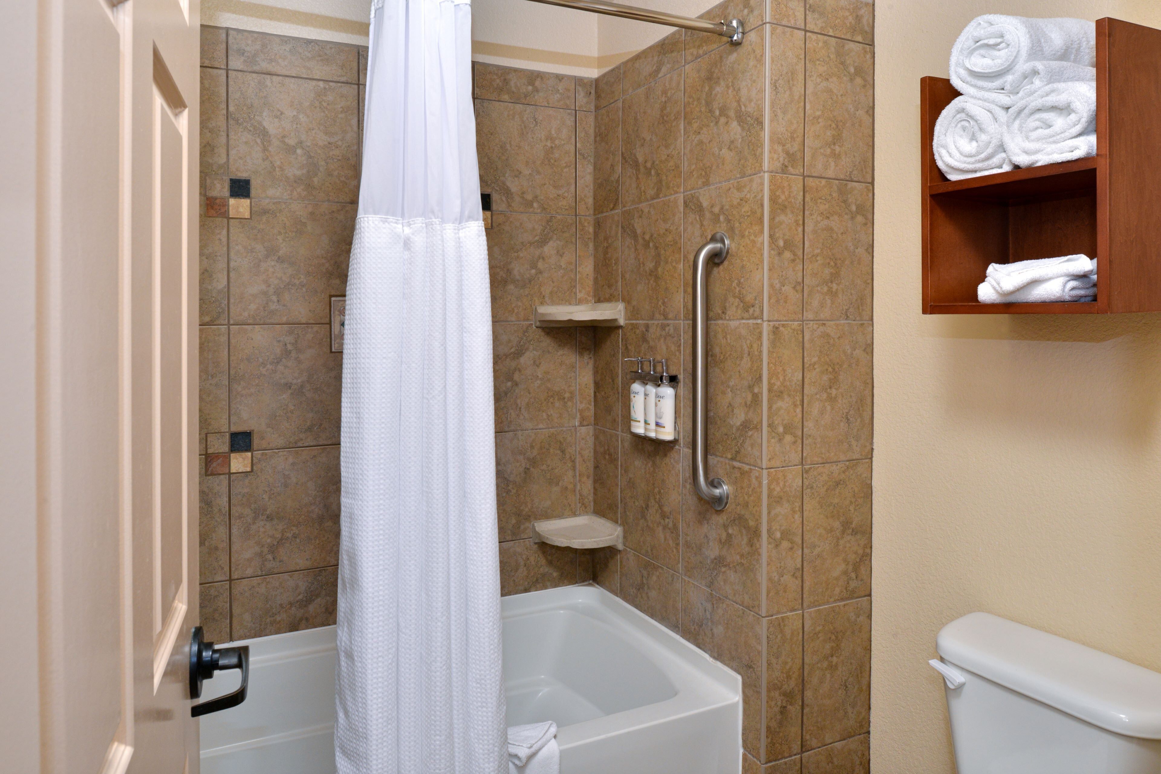 A bathroom with a bathtub, a shower curtain, a grab bar, a shelf with toiletries, and a towel rack.