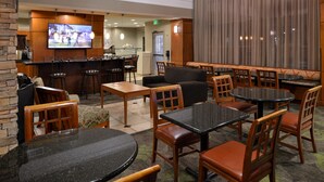 A hotel lobby with multiple seating areas, including round tables and sofas, a bar area with a television, and a large window with curtains. - Staybridge Suites Las Cruces by IHG (Las Cruces)
