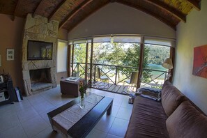 Een gezellige woonkamer met een stenen openhaard, een bank, een salontafel en een balkon met uitzicht op bomen.
