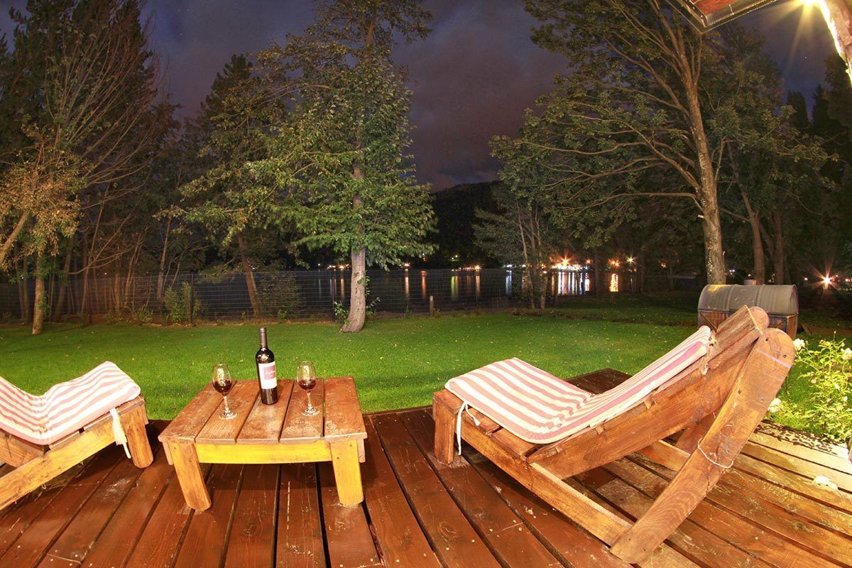A wooden deck with two lounge chairs and a table, a bottle of wine, and a glass of wine.