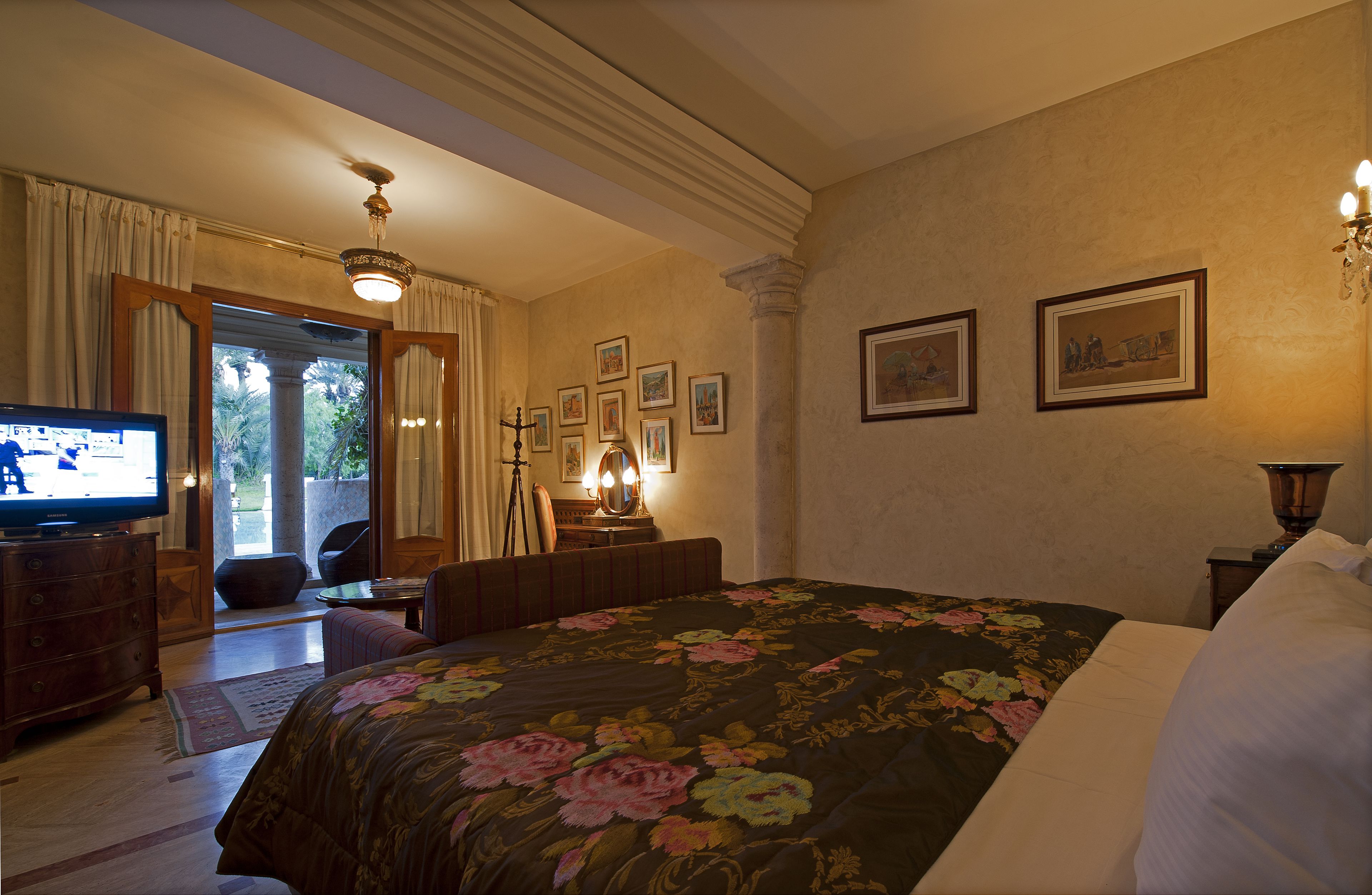 Habitación de hotel con cama, televisor, escritorio con lámpara y cuadros en la pared.