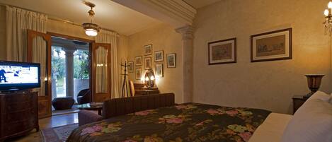 Habitación de hotel con cama, televisor, escritorio con lámpara y cuadros en la pared.