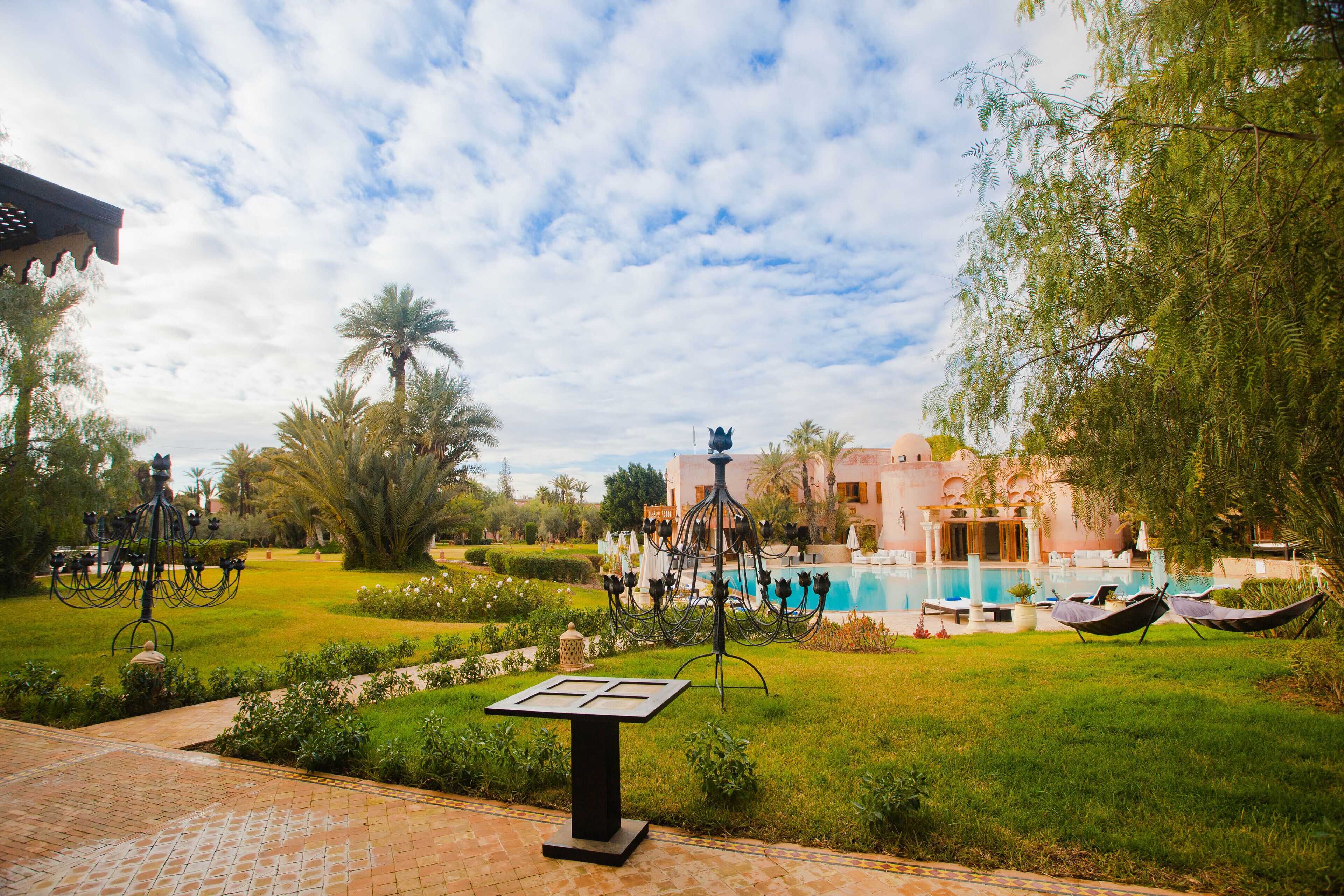 A courtyard with a pool, palm trees, and a building with arches.