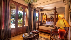 A bedroom with a four-poster bed, a wooden nightstand, a table with a lamp, and a view of the outside through a door. - Palais Mehdi (Marrakech)