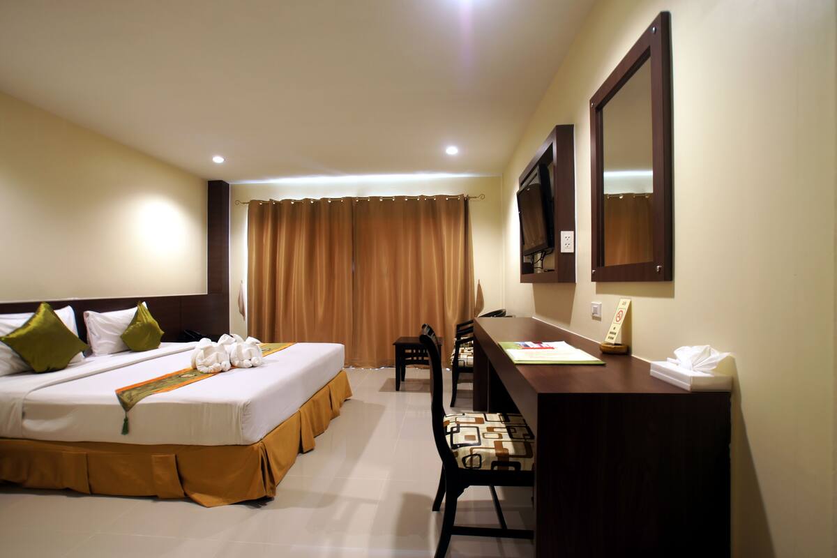 A hotel room with a bed, desk, chairs, and a TV.