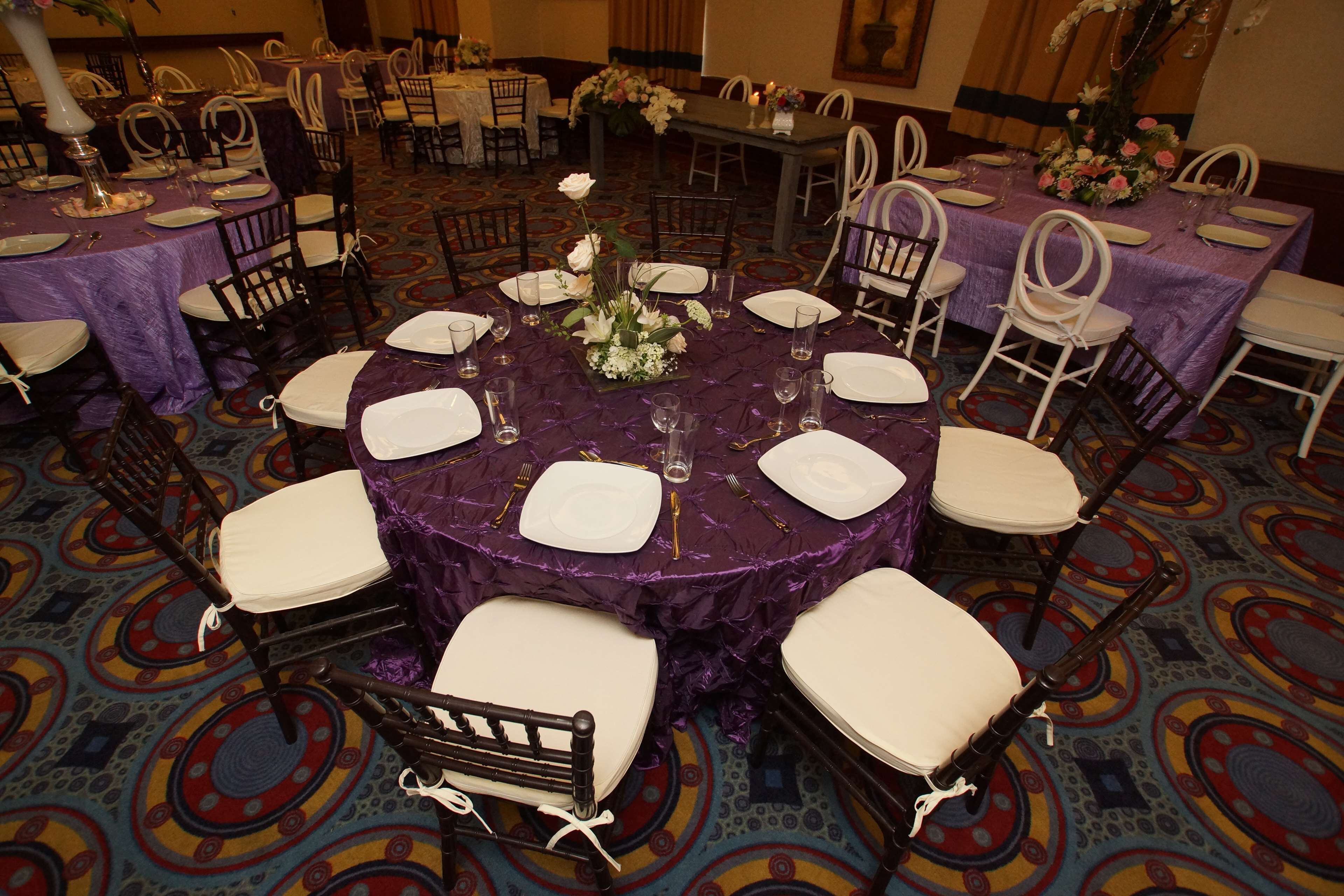 A banquet hall with round tables covered in purple tablecloths, white chairs, and floral centerpieces.