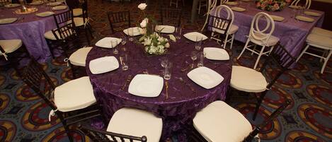 A banquet hall with round tables covered in purple tablecloths, white chairs, and floral centerpieces.