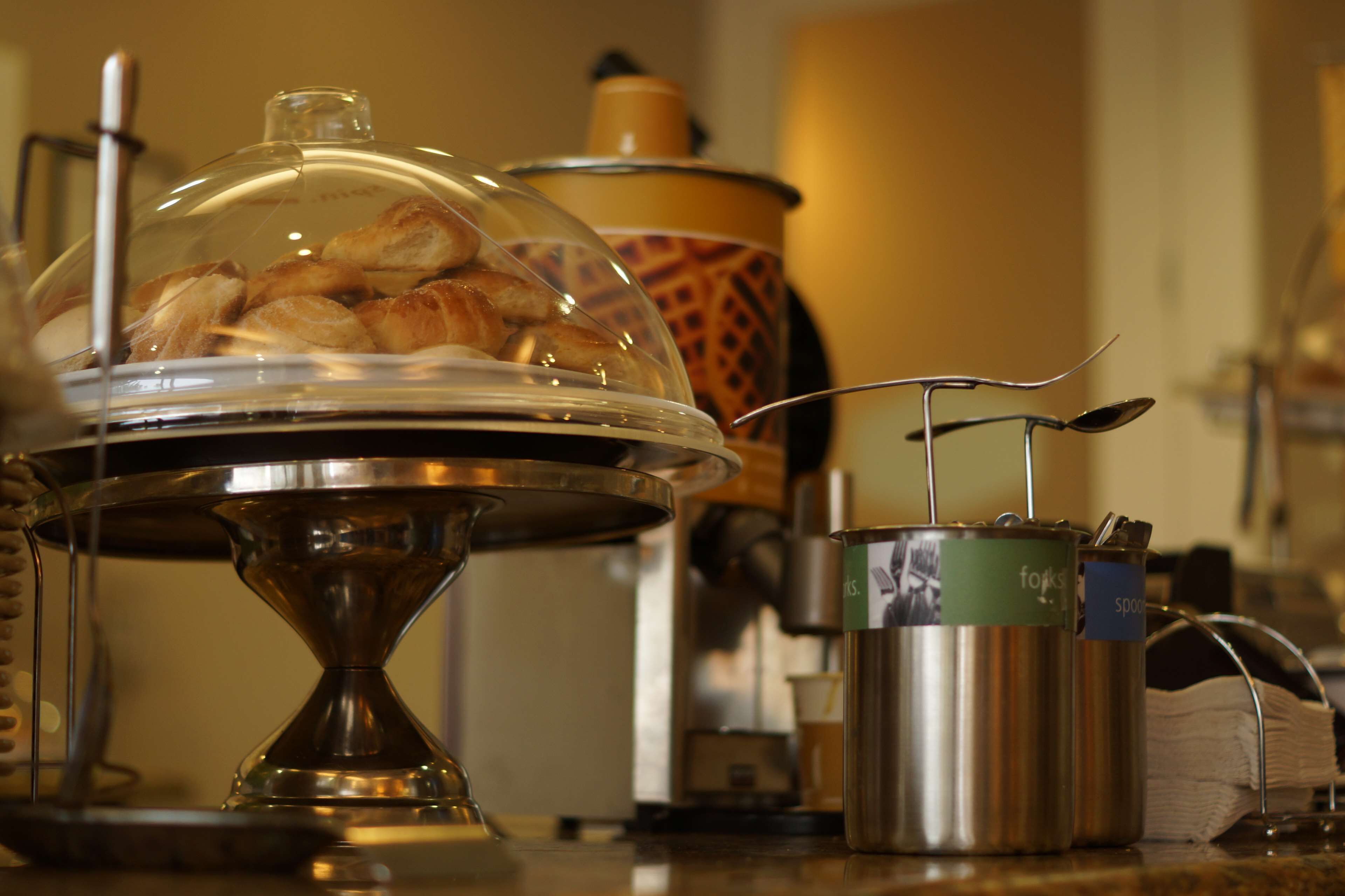 Un buffet avec un plat de service couvert, une machine à café et un petit récipient en métal muni d’une étiquette.