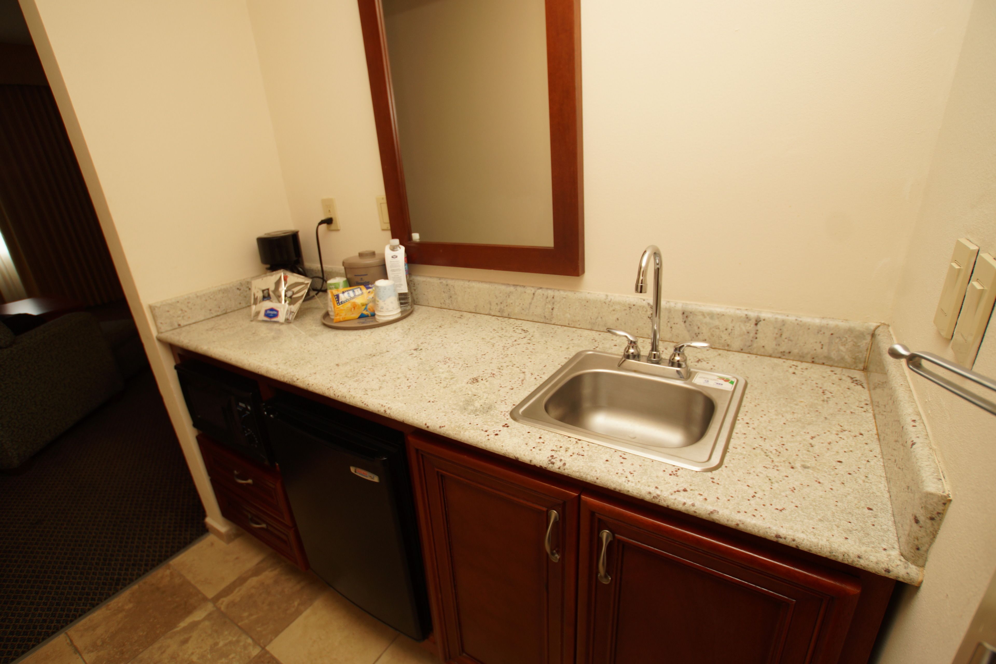A kitchen with a granite countertop, stainless steel sink, and wooden cabinets.