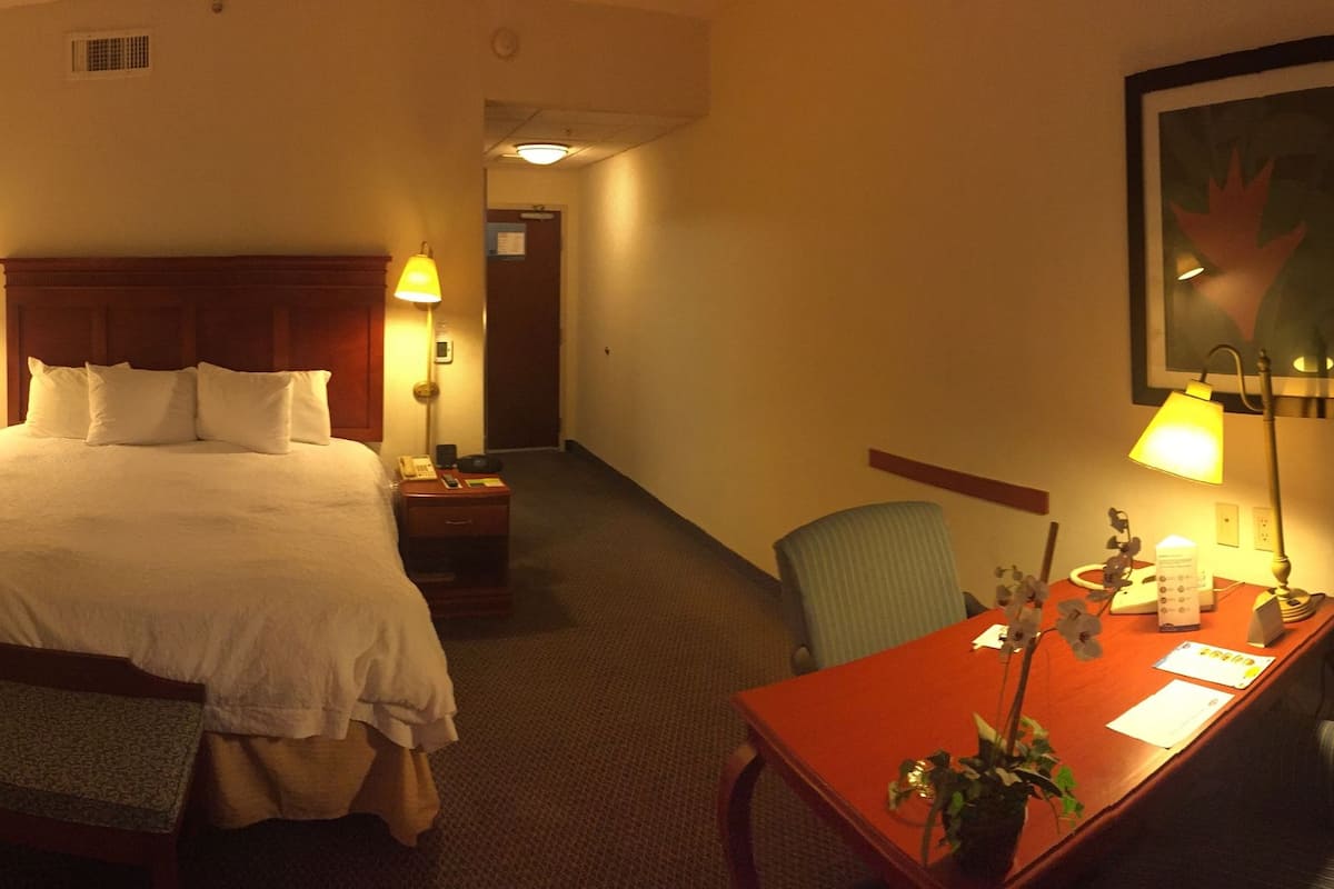 A hotel room with a bed, bedside table, lamp, desk, chair, and a television.