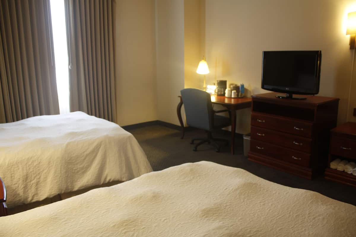 A hotel room with two beds, a desk with a chair, a television, and a dresser.