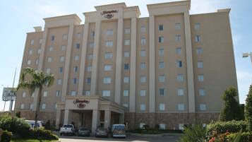 A multi-story hotel with a central entrance, several parking spaces, and surrounding greenery.