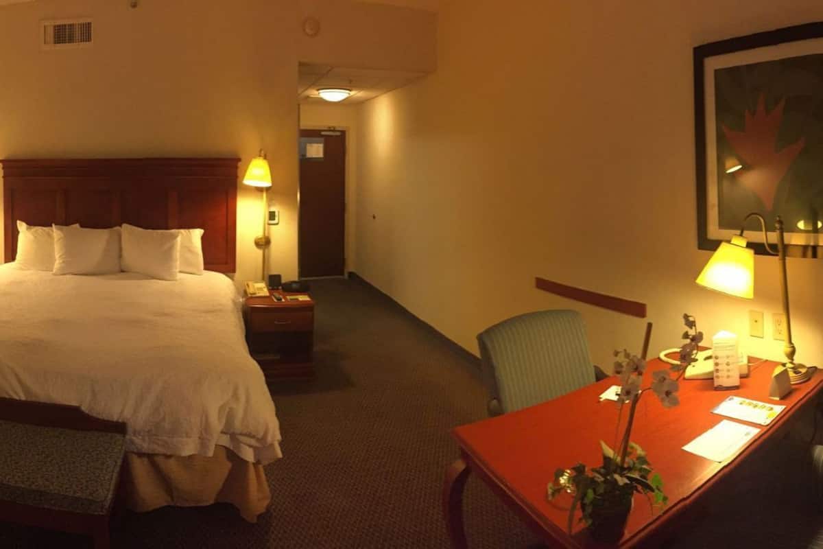 A hotel room with a bed, bedside table, desk, chair, lamp, and a television.