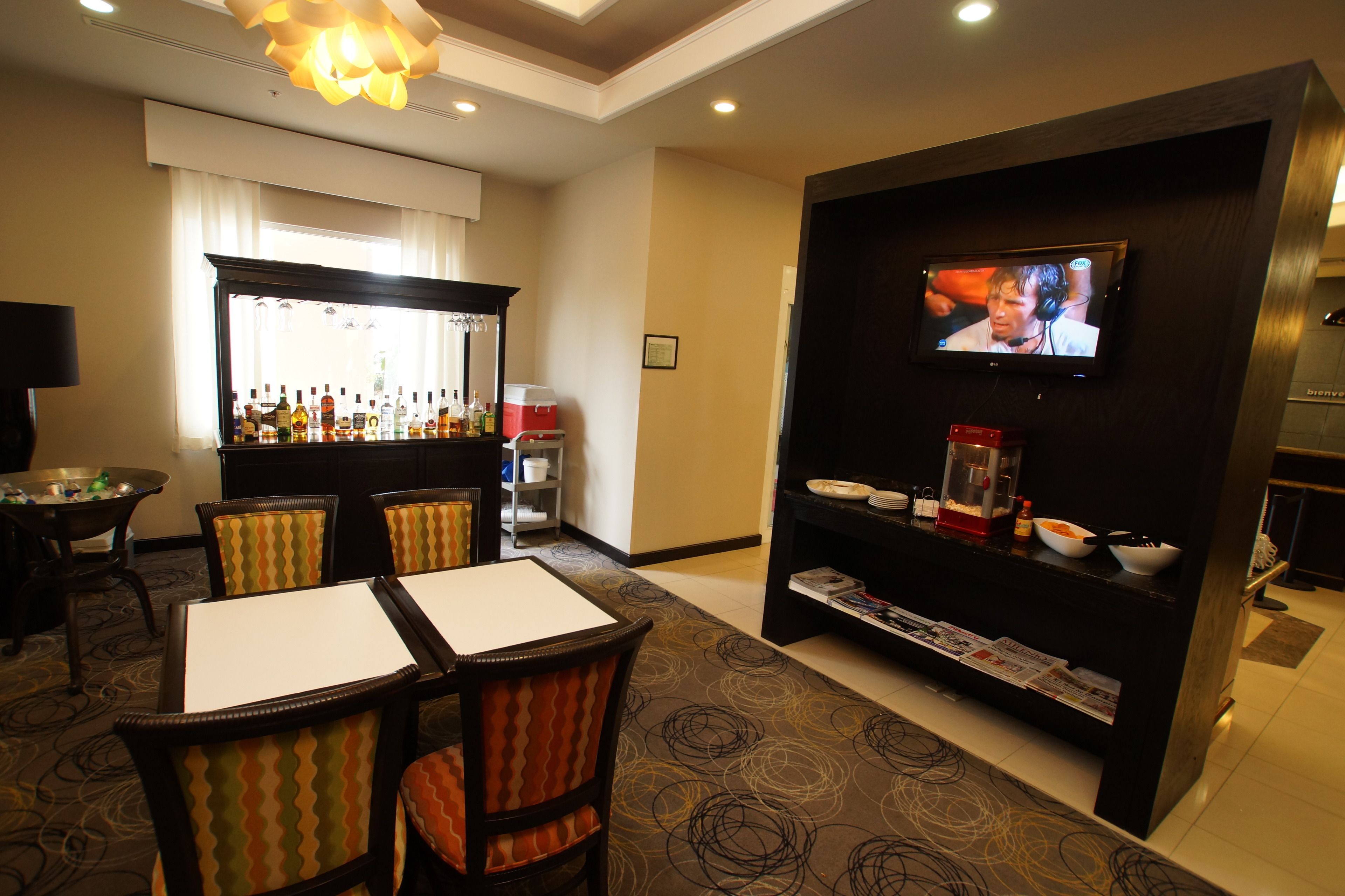 A hotel room with a bar area, a television, and a dining table with chairs.
