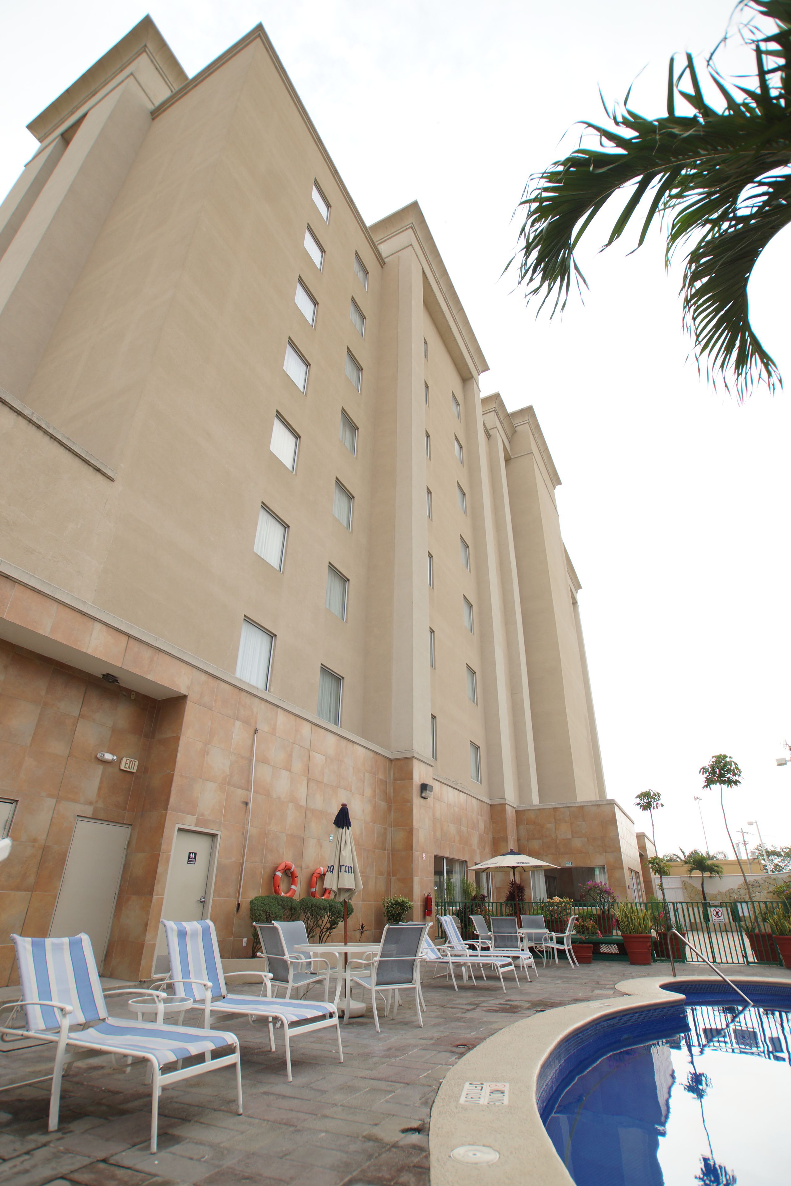 A hotel with a pool area, lounge chairs, and a tall building with multiple windows.