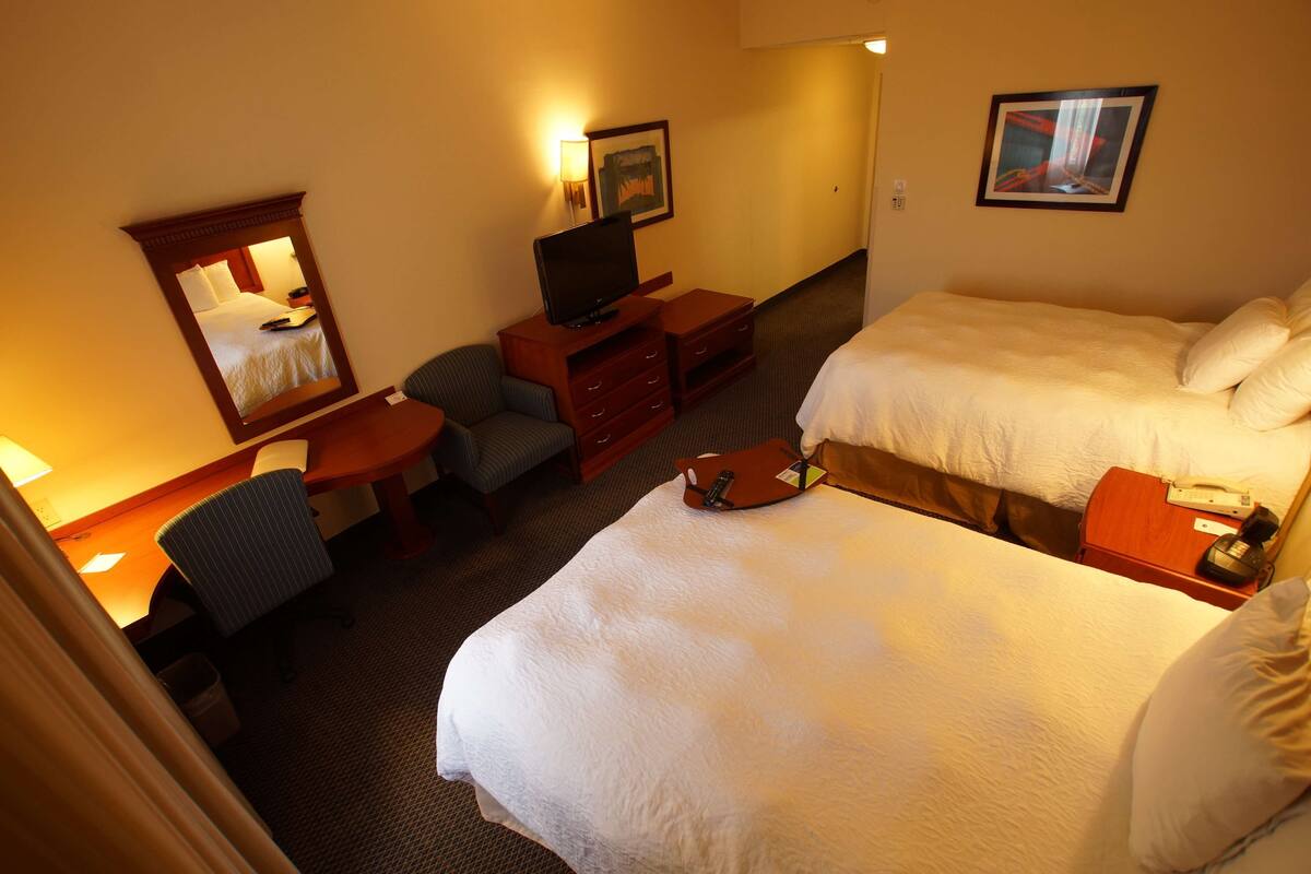 A hotel room with two beds, a desk, a chair, a television, and a mirror.