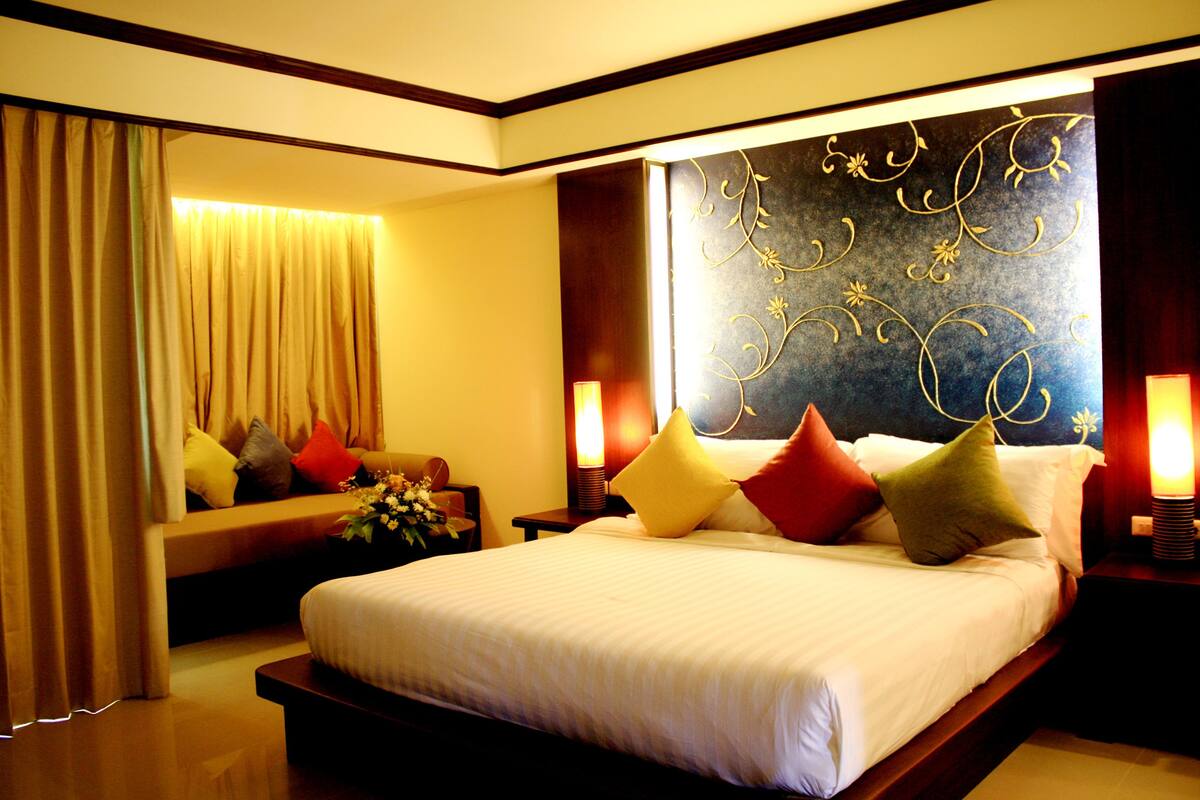 Habitación de hotel bien iluminada con una cama grande, una mesita de noche con lámpara y un panel decorativo en la pared.