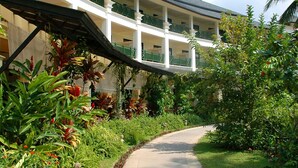Un sendero curvo que conduce a un edificio con varios balcones, rodeado de exuberante follaje y plantas tropicales.
