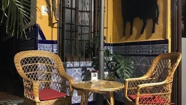 A patio area with wicker chairs and a small table, a decorative wall with a bull sculpture, and a metal gate. - Hotel Nova Centro (Jerez de la Frontera)
