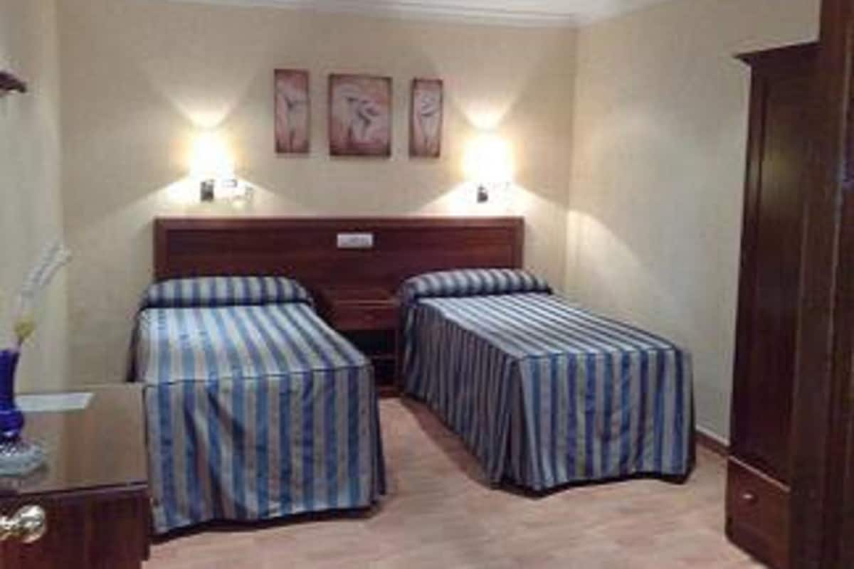 Een hotelkamer met twee enkele bedden, een houten garderobe en een nachtkastje met een lamp.