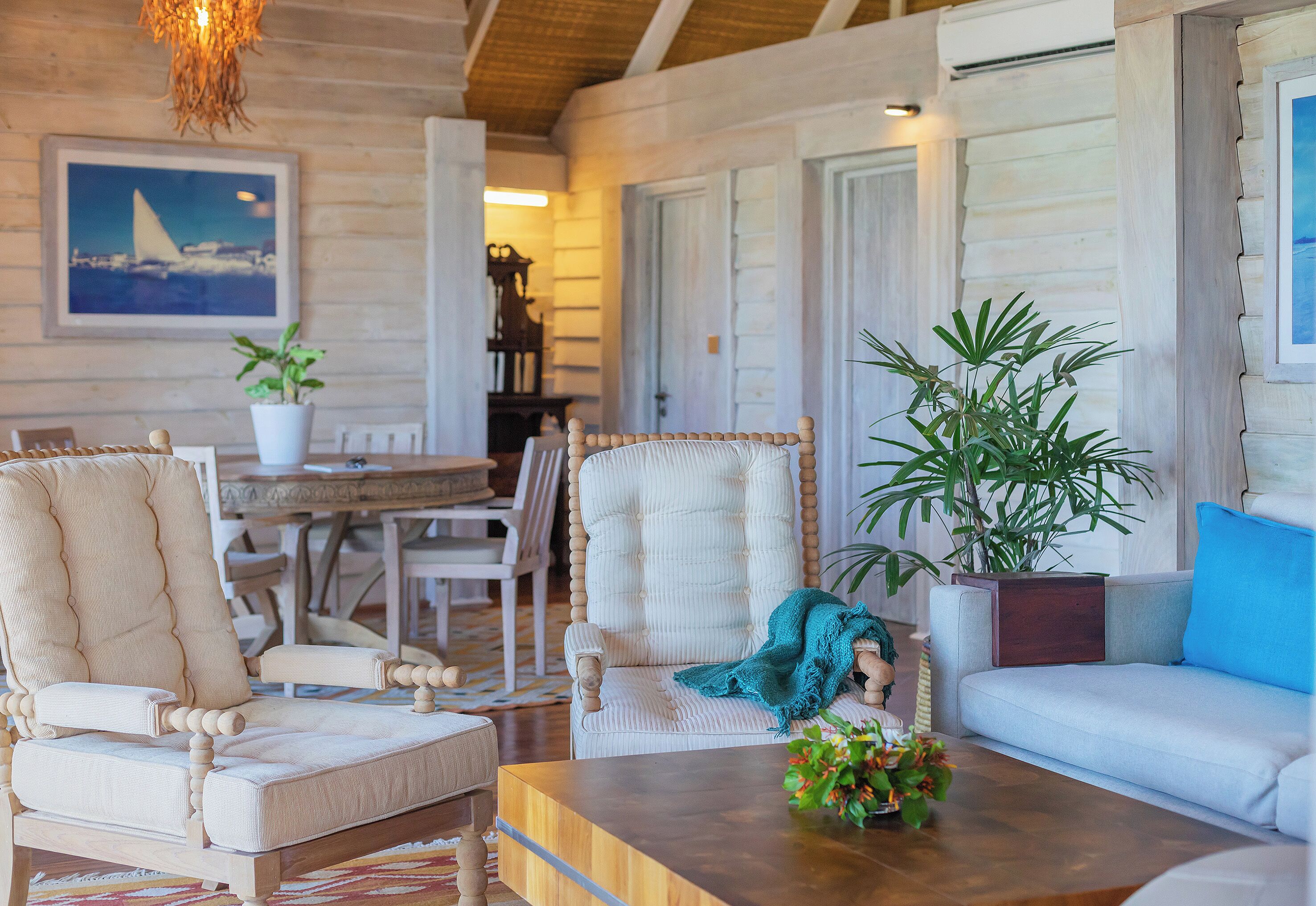 Une pièce chaleureuse avec un plafond en bois, une table à manger, deux chaises, un canapé et une table basse agrémentée d’une plante.