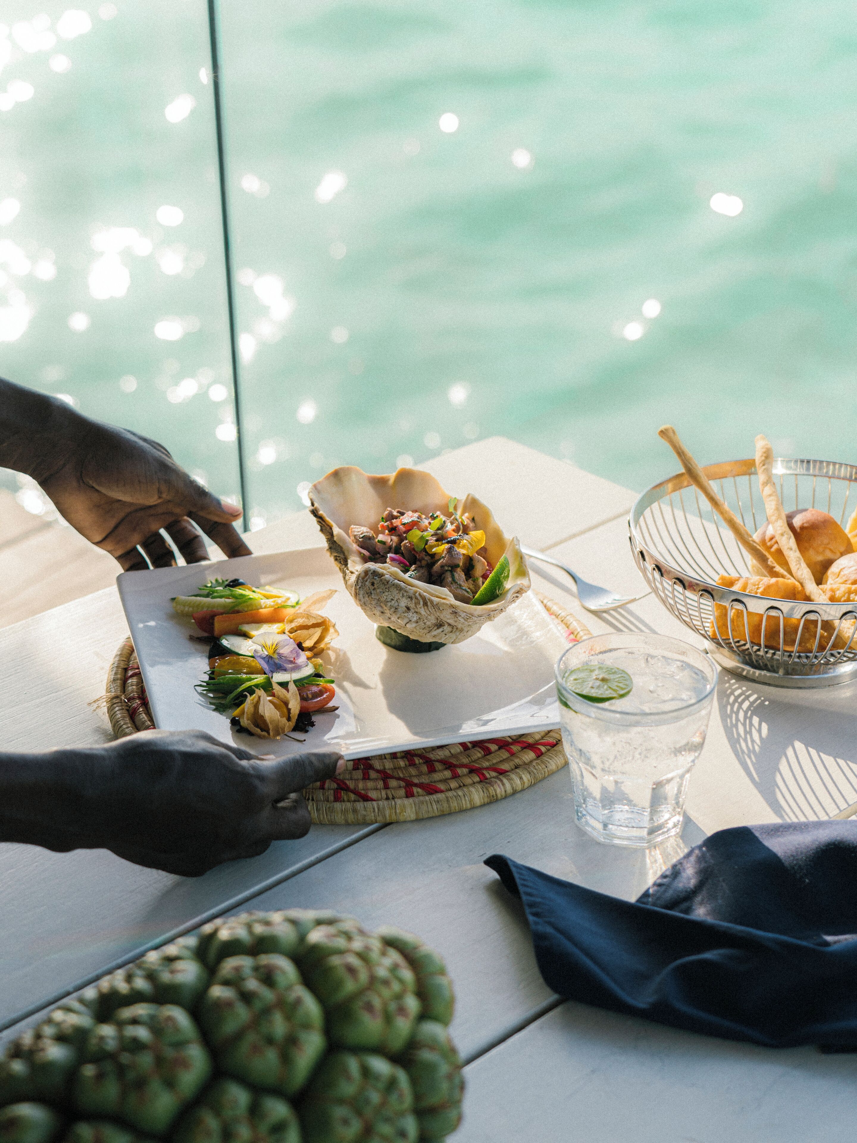 A table with food items, a glass of water, and a view of the water.