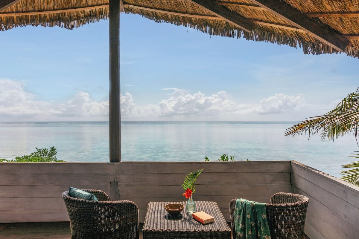 Ein Balkon mit Korbmöbeln, einem Tisch mit einer Schale und einem Buch, und Blick aufs Meer.