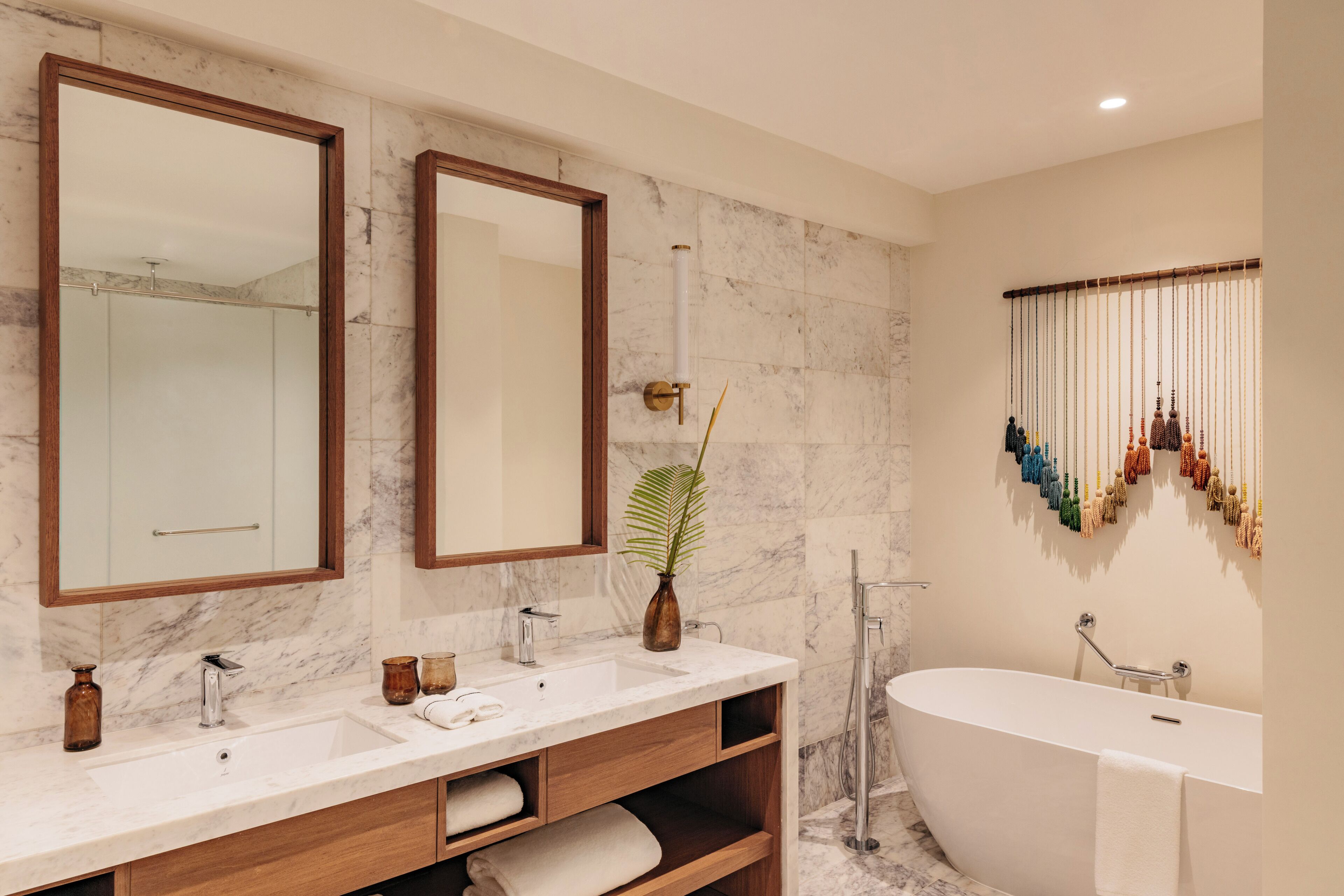 Une salle de bain moderne avec deux grands miroirs, une baignoire sur pieds et un mur recouvert de carreaux de marbre.