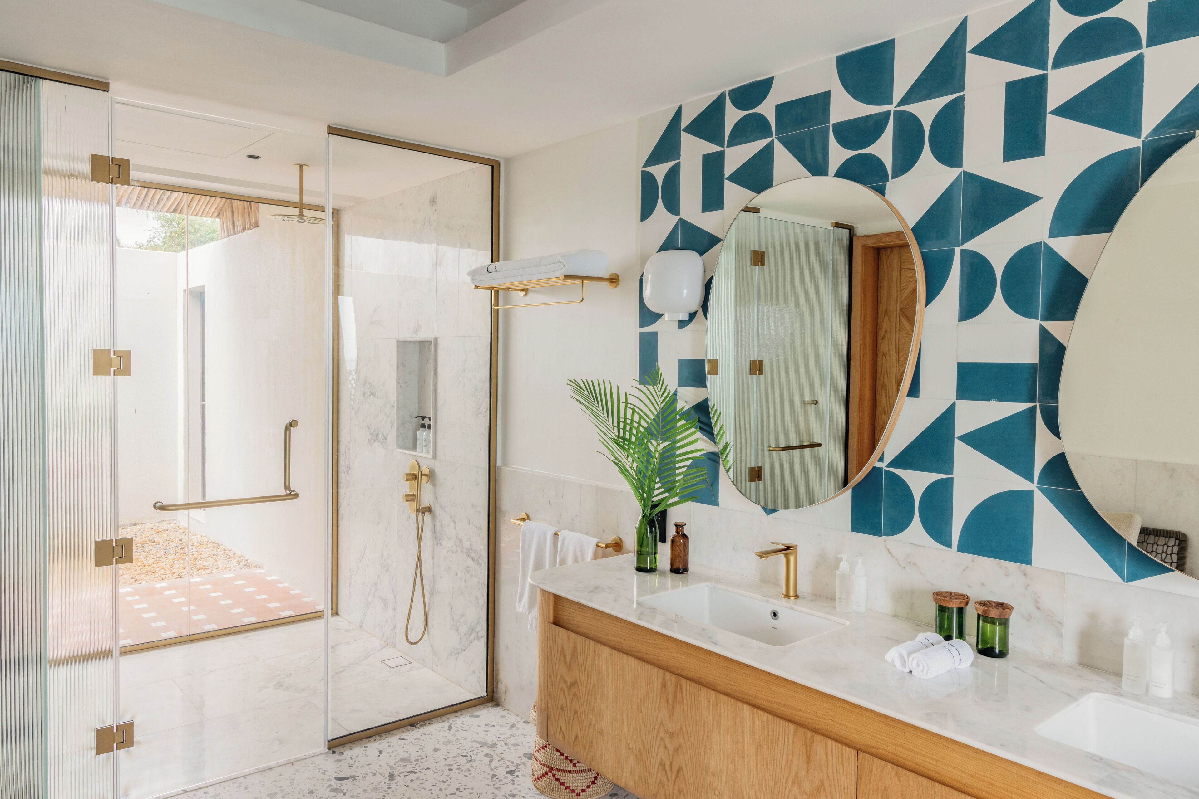 A modern bathroom with a glass shower enclosure, a marble sink, and a geometric tile backsplash.