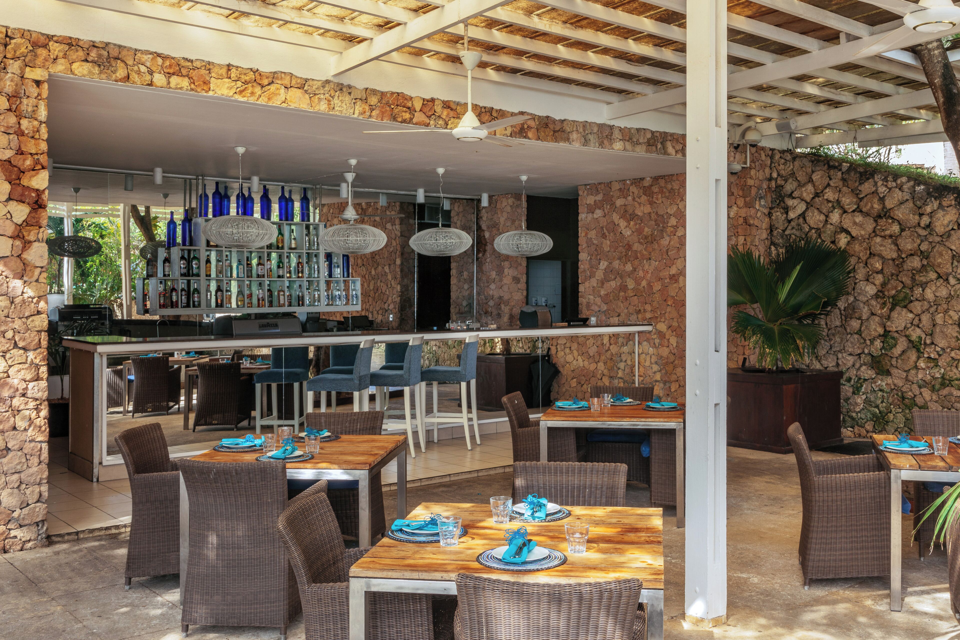 An outdoor dining area with stone walls, wicker furniture, and a bar with blue bottles.