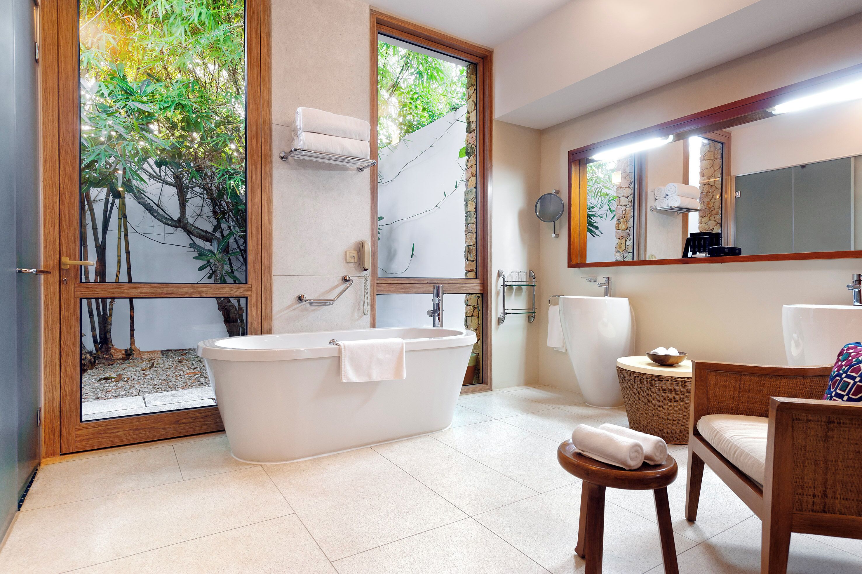 A modern bathroom with a freestanding bathtub, a large mirror, and a wicker chair.
