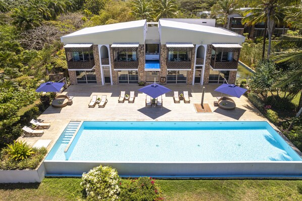 A modern two-story house with a swimming pool, sun loungers, and umbrellas.