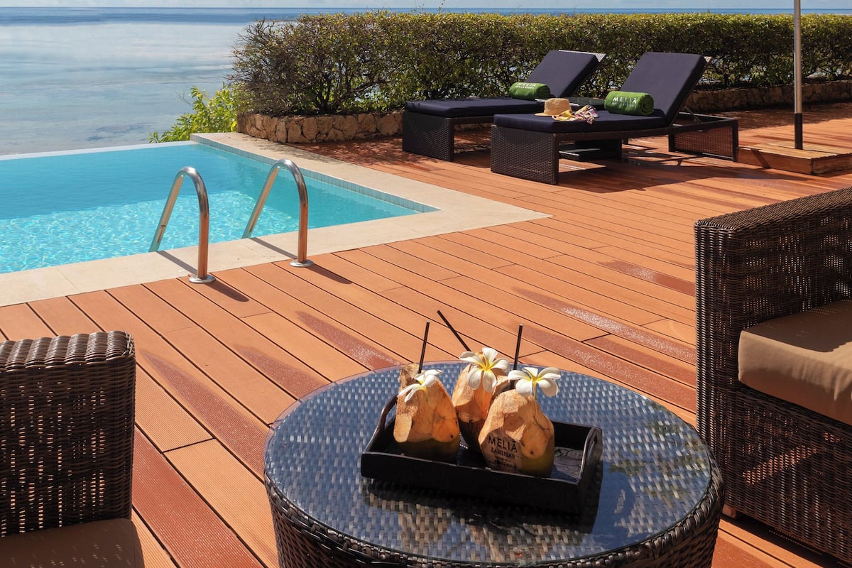 Ein Poolbereich mit Liegestühlen, einem Tisch mit Snacks und Blick aufs Meer.