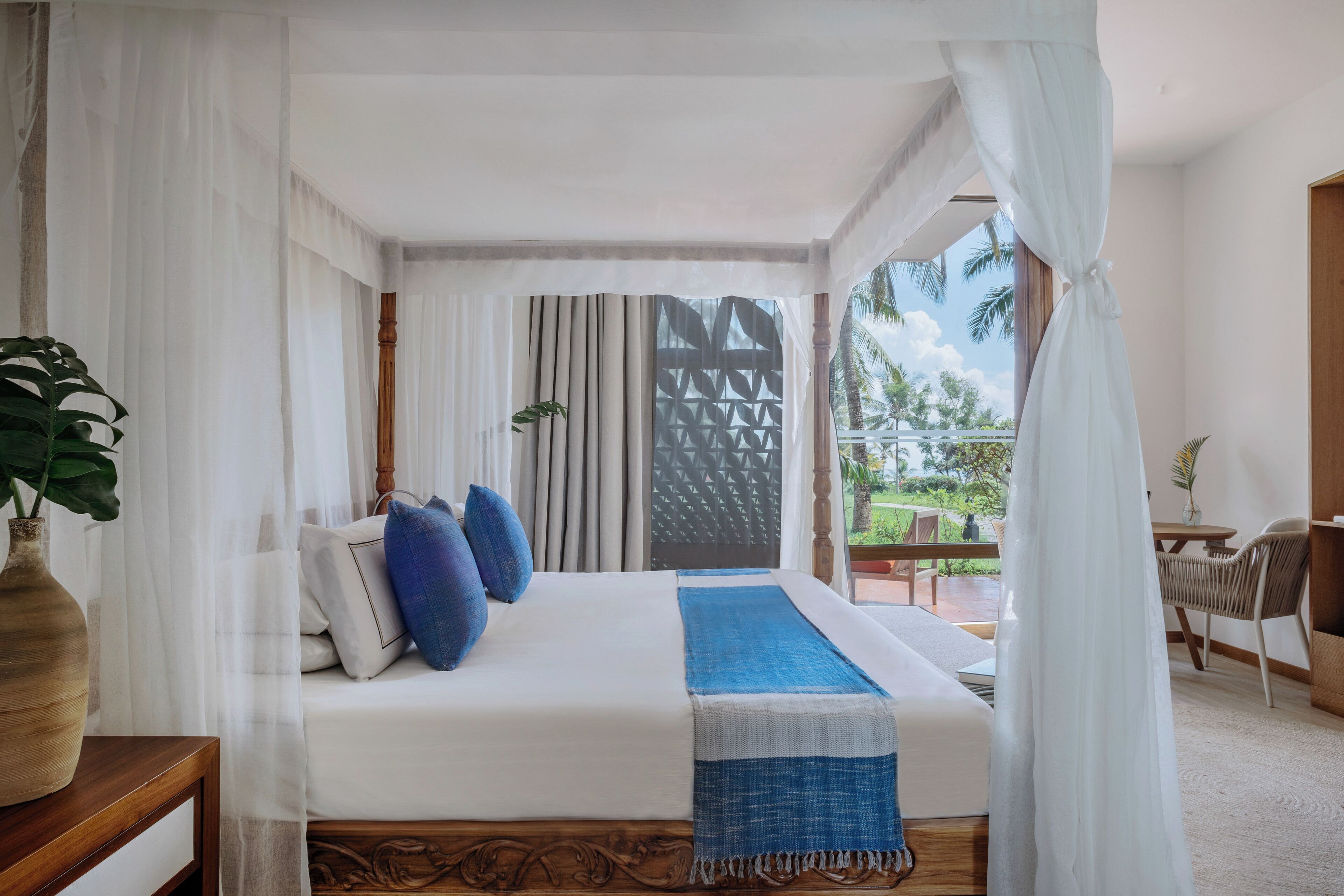 Un dormitorio con cama, cortinas blancas, vistas al exterior y cabecera de madera.