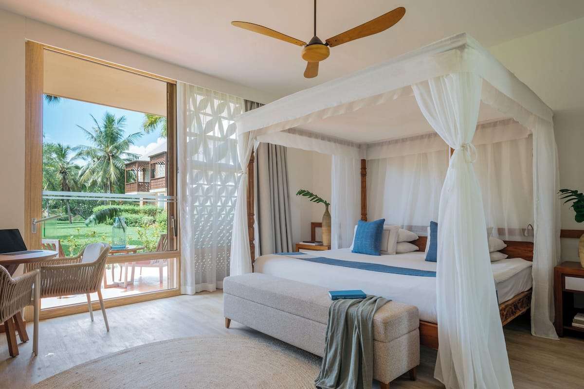 Ein Schlafzimmer mit Baldachinbett, Schreibtisch und Blick ins Freie.