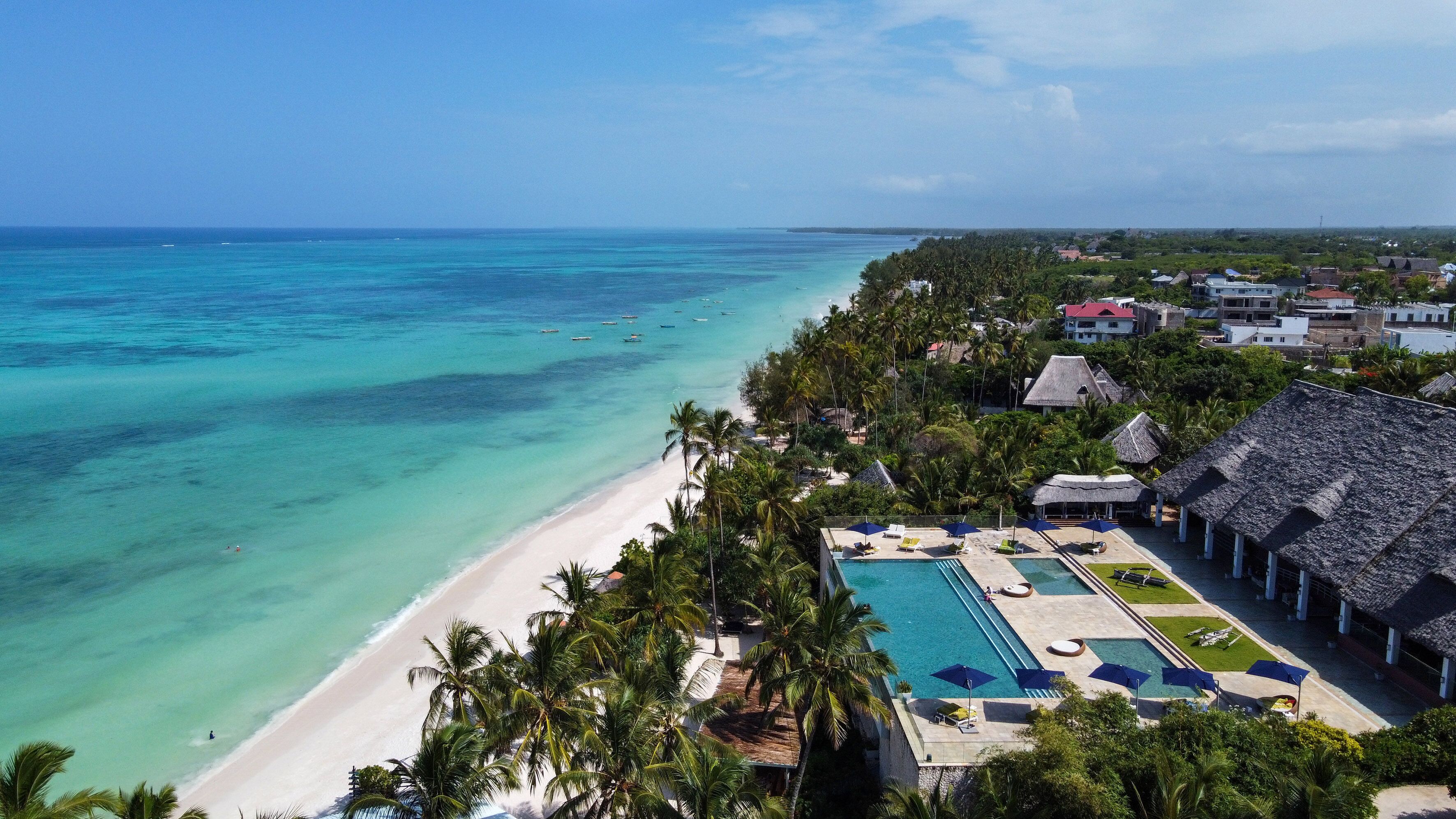A resort with a beach, pool, and thatched-roof buildings.