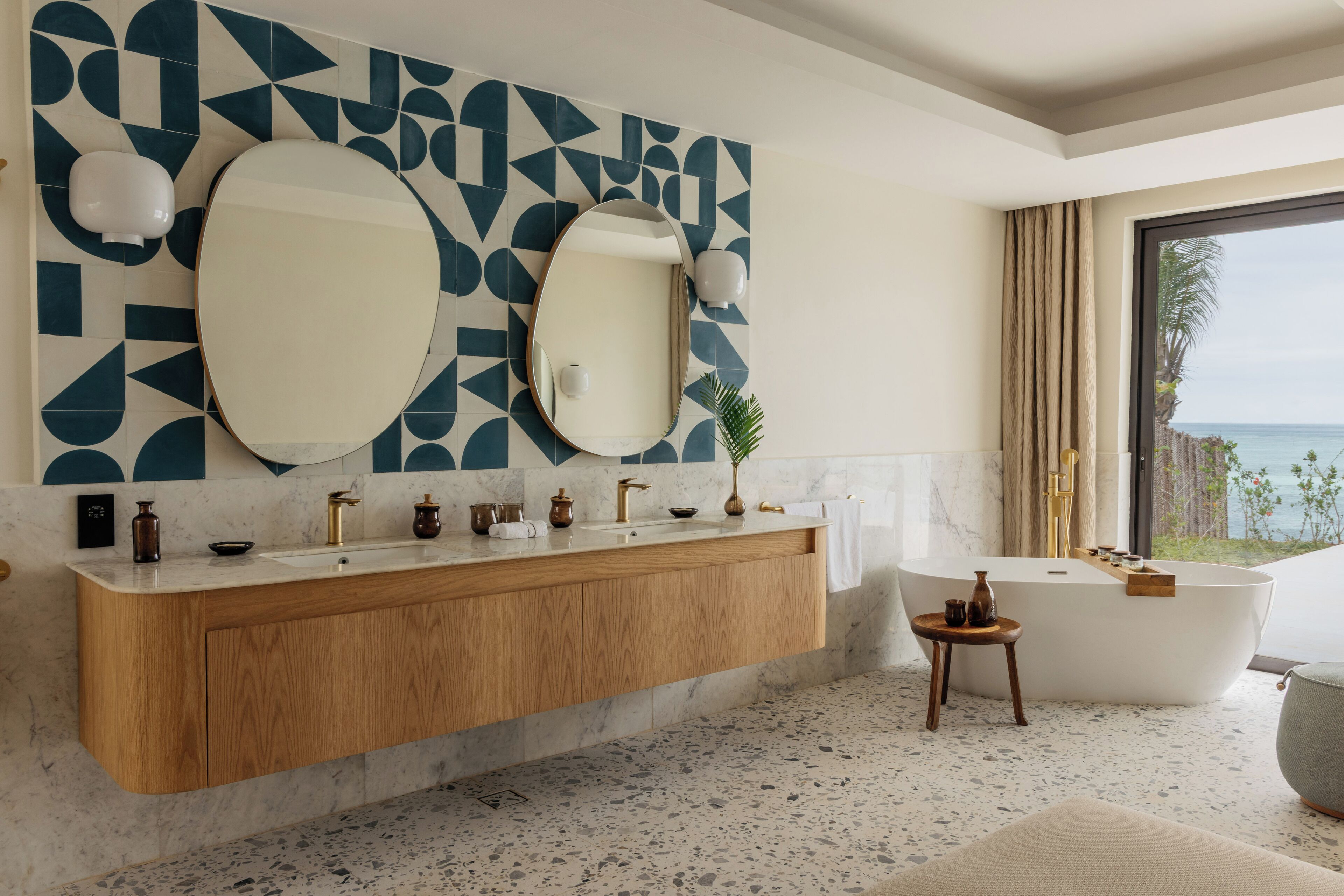 Un baño moderno con una bañera independiente, un espejo grande y un salpicadero de azulejos geométricos.