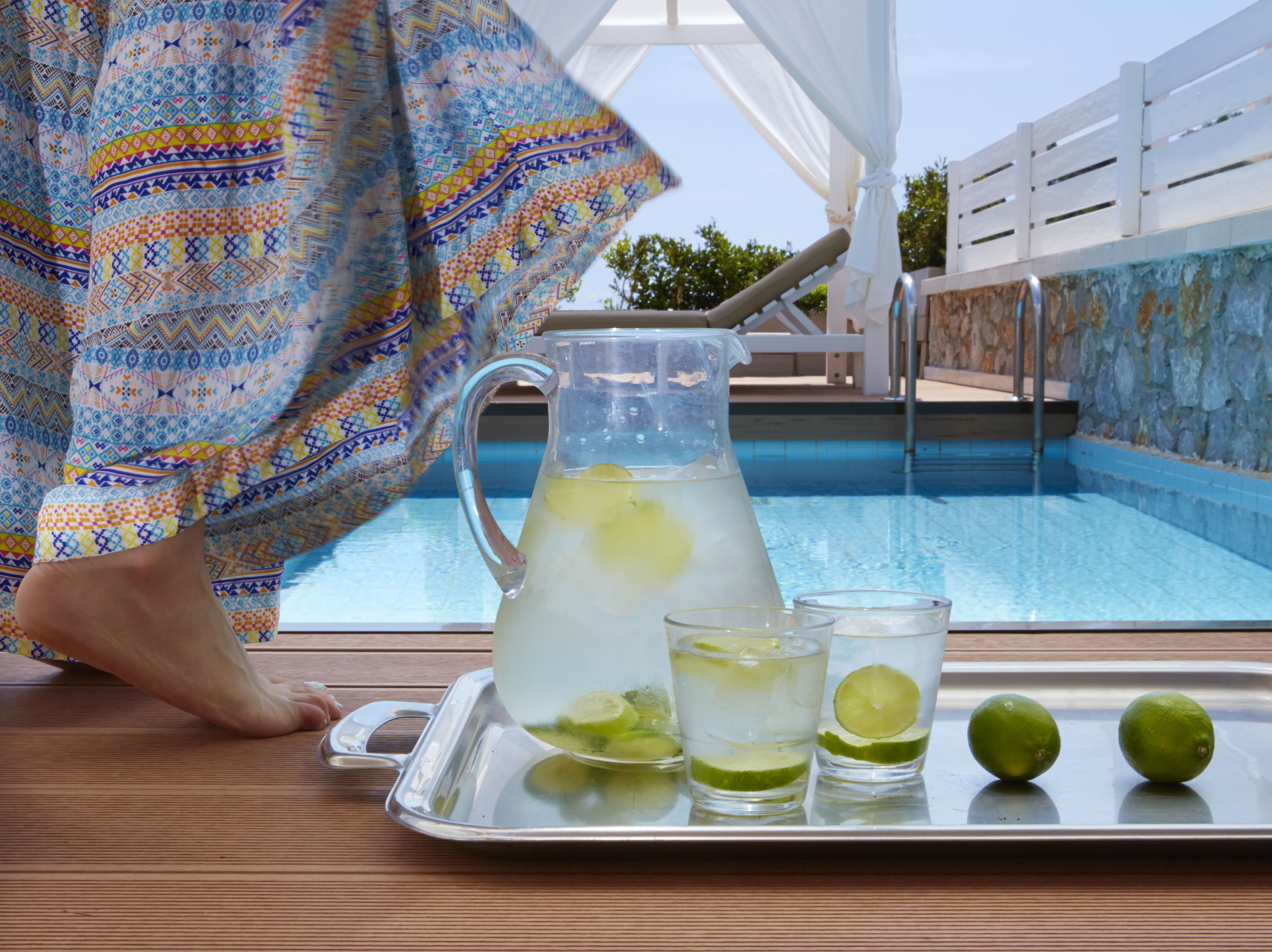 A poolside setting with a pitcher of lemonade, two glasses, and limes on a tray.