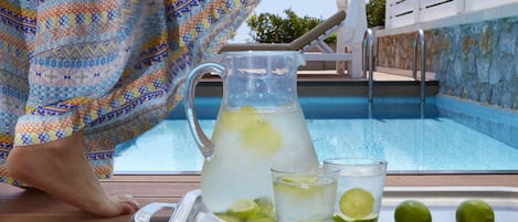 A poolside setting with a pitcher of lemonade, two glasses, and limes on a tray.