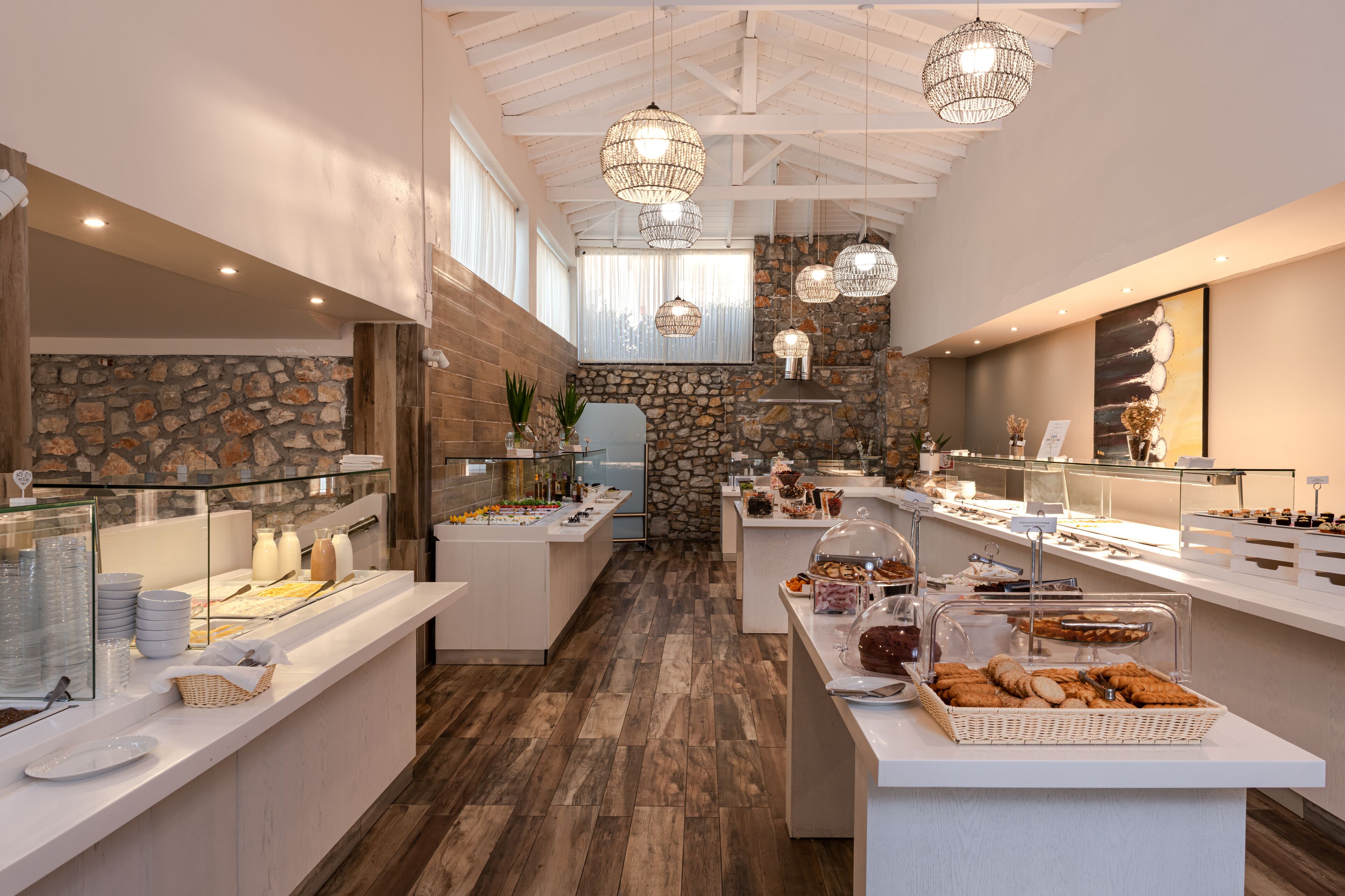 A modern breakfast buffet with stone walls, wooden flooring, and pendant lighting.