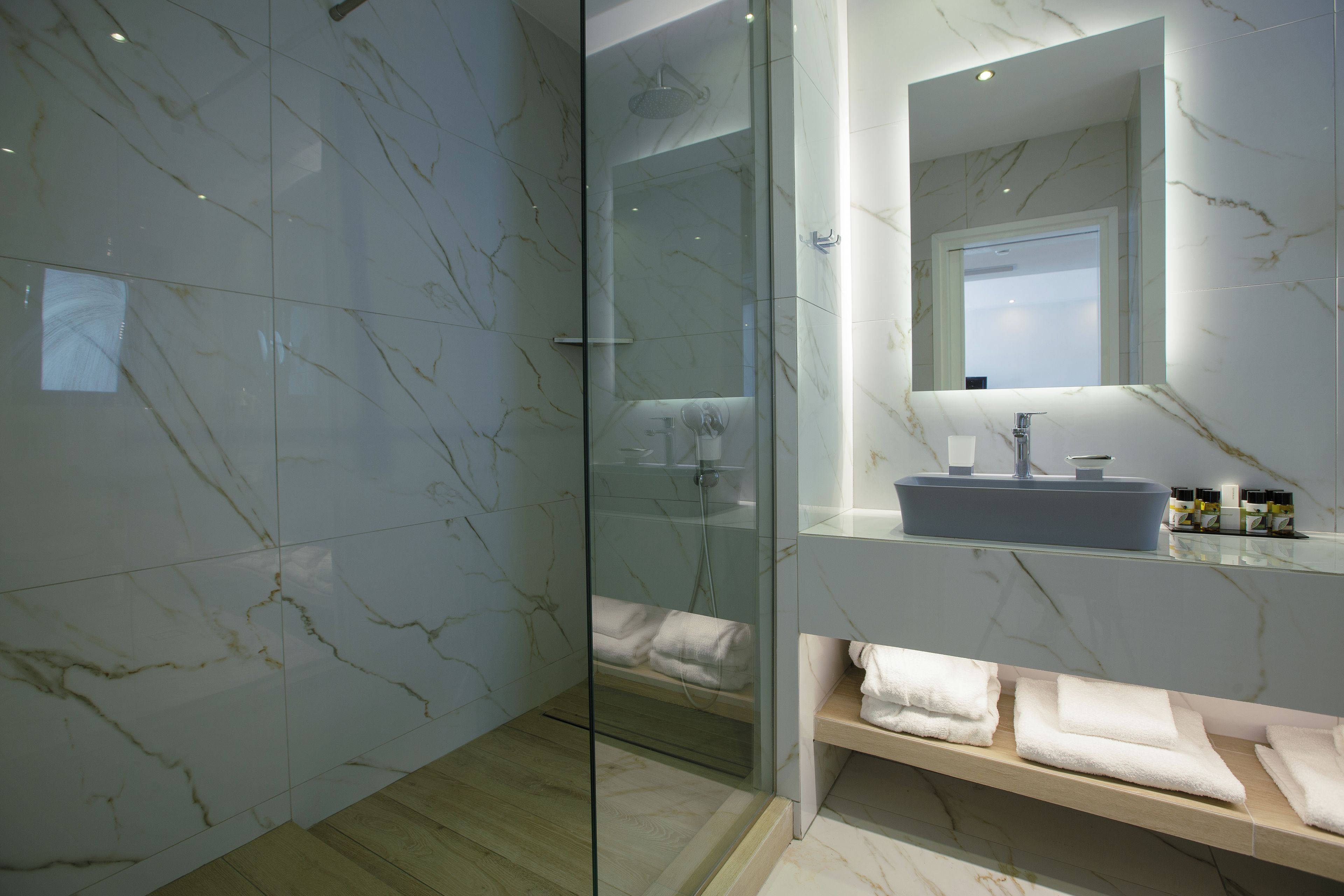 A modern bathroom with a glass-enclosed shower, marble walls, and a vanity with a sink and towel rack.