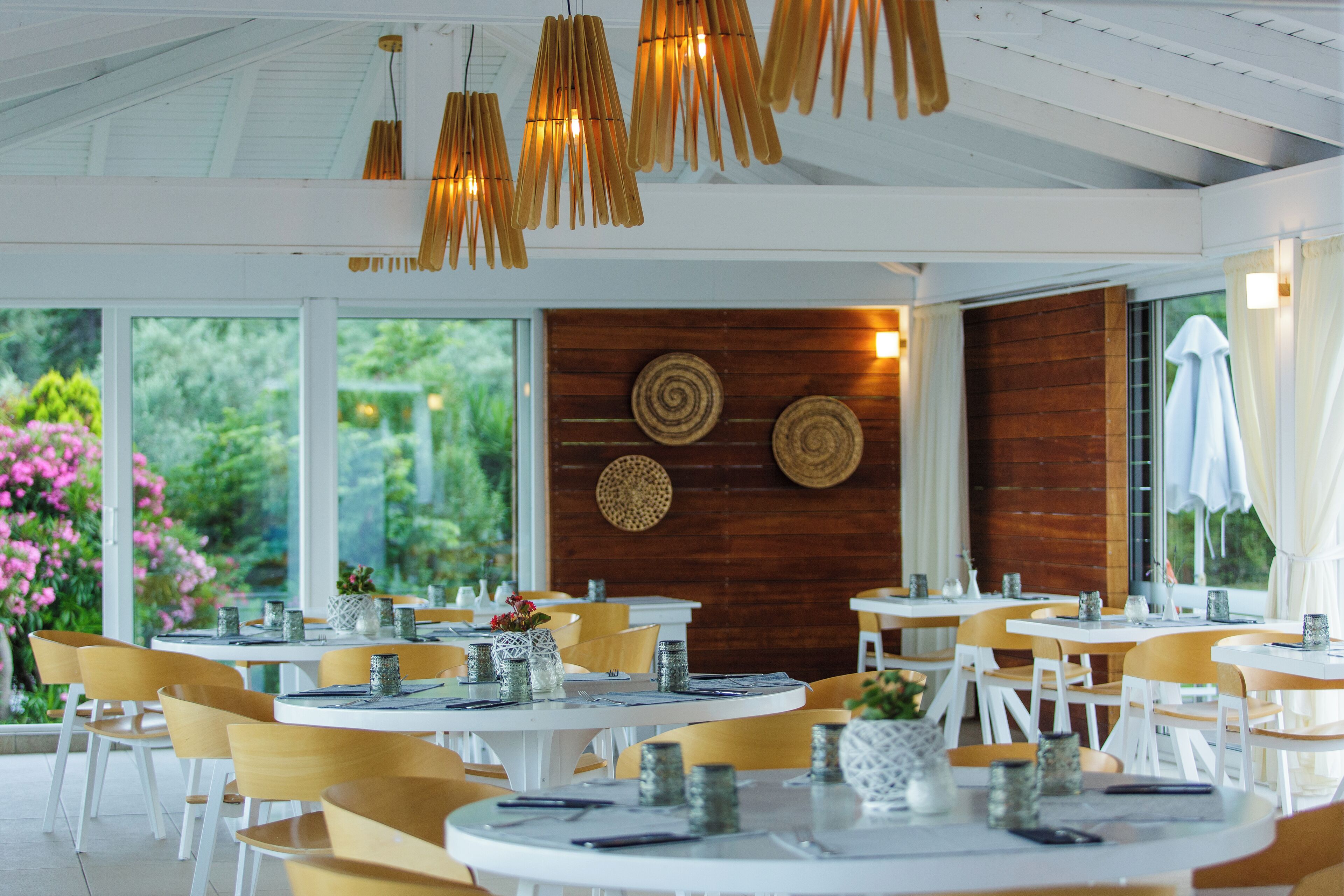 A restaurant with round tables and chairs, wooden accents, and a view of greenery.