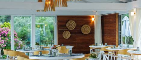 A restaurant with round tables and chairs, wooden accents, and a view of greenery.