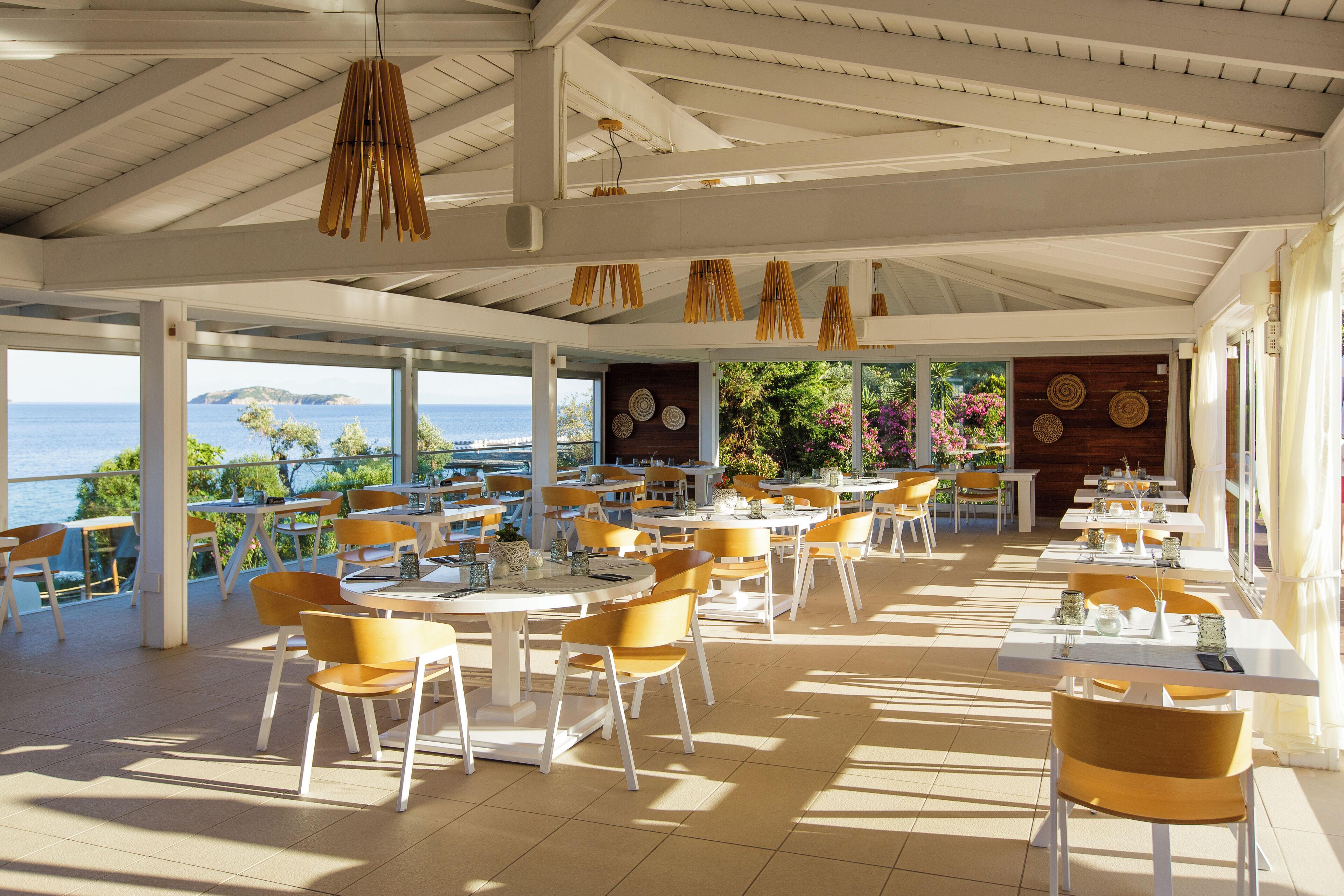 A spacious outdoor dining area with white tables and yellow chairs, overlooking a scenic view of the sea.