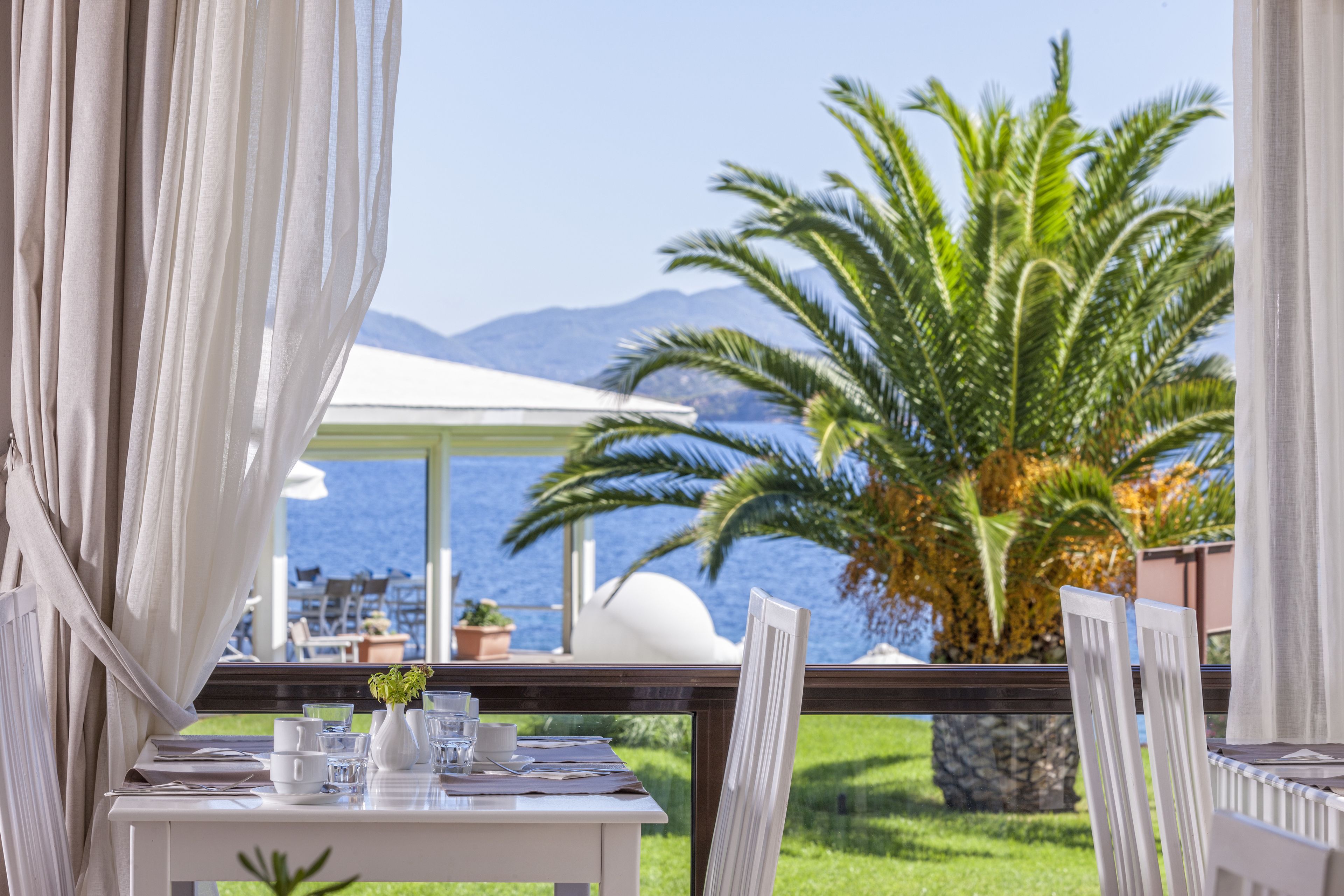 A table set for dining with a view of the sea and palm trees.
