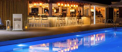 Zona de bar junto a la piscina con asientos y un cartel que dice "KASSANDRA BAY".