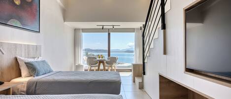 A modern hotel room with two beds, a large TV, a balcony with a view of the sea, and a staircase.