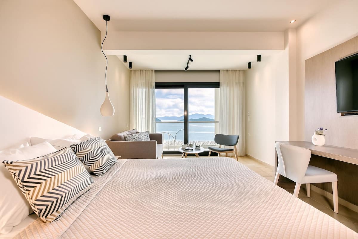A modern hotel room with a large bed, a desk, and a view of the sea.